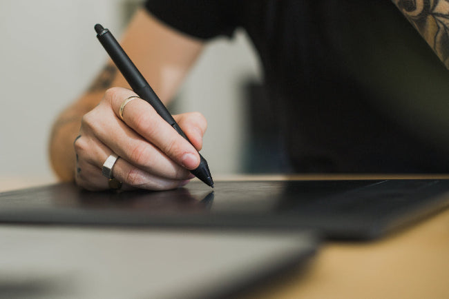 Person using a stylus on a digital drawing tablet with a blurred background